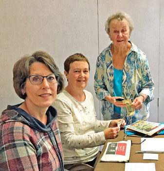Pam Schulstad (standing) is stocking up on Crystal Cards with the help of volunteers Karen MacFarlane and Carol Norvet.
