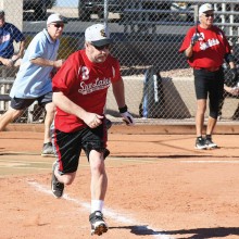 Tim Baldwin sprints toward first base in a recent contest. Umpire Ken Brenden follows the play while on deck hitter, TJ Tjernlund, looks on. (Courtesy of Core Photography, LLC).