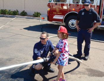 Firefighter Craig Daniels lets this young girl get a chance to put out the “fire.” Firefighter Brandon Johnson watches.